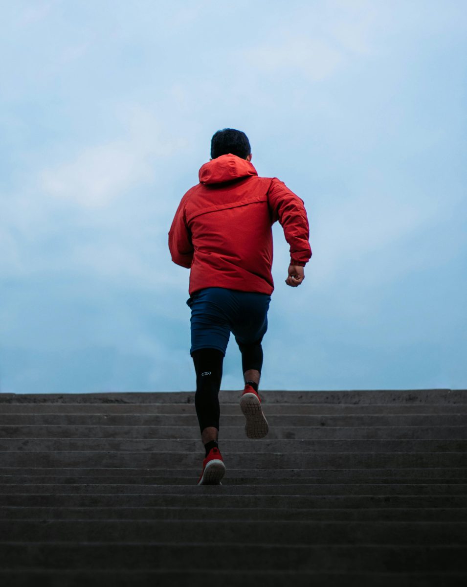 Man in Red Hooded Jacket Running on Concrete Stairs