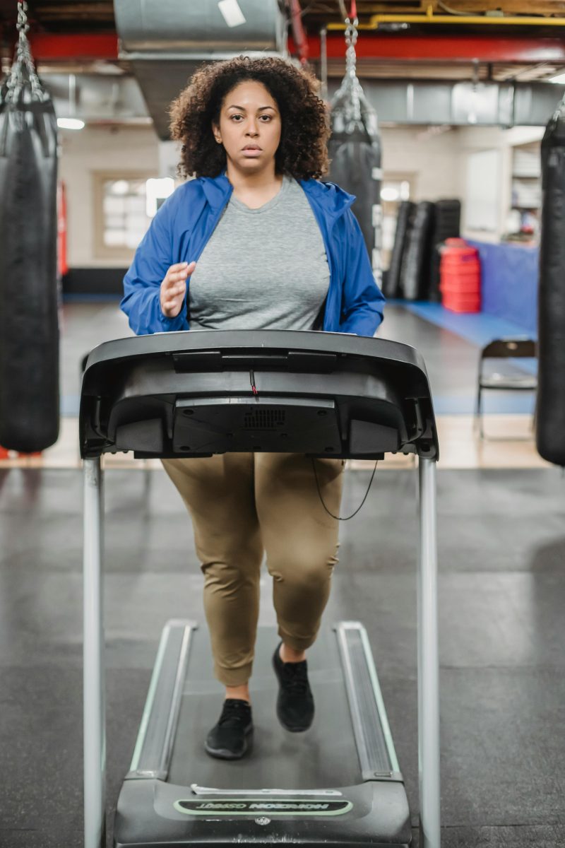 Full body of overweight female running on treadmill during workout and looking at camera